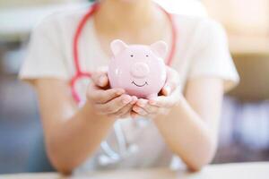 Closeup and crop hands of medical student holding piggy bank on blurred background. photo