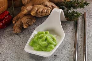 A bowl of green sauce next to a spoon and some ginger photo