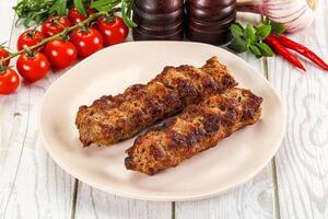 Two meat skewers on a plate with tomatoes and herbs photo
