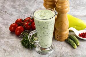 A glass of green smoothie with tomatoes, cucumbers and other ingredients photo