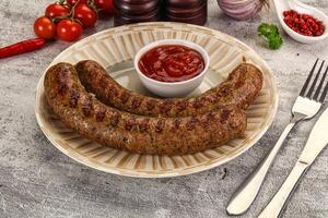 Two sausages on a plate with a tomato and a fork photo