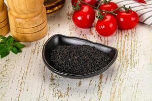 A bowl of black seeds on a table next to a bottle of olive oil photo