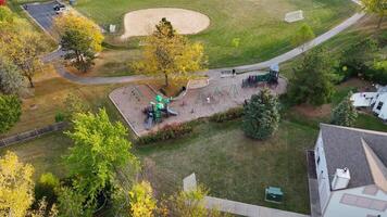 Aerial View of Community Playground and Park. Aerial shot of a vibrant community park featuring a playground, swings, walking paths, sports fields, and lush greenery. video