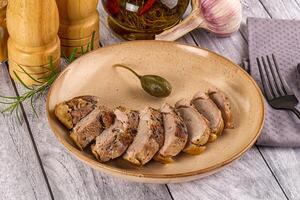 A plate of meat on a wooden table with a knife and fork photo