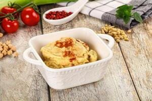 A bowl of hummus with a spoon and a bowl of tomatoes photo