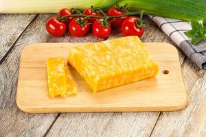 A piece of cheese on a cutting board next to a tomato photo