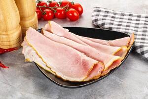 Sliced ham on a black plate with a checkered cloth photo