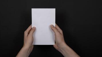 Hands holding blank white paper against black background. photo