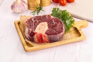 A piece of meat on a cutting board with a tomato and garlic photo