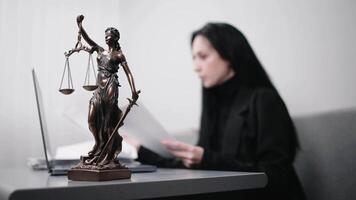 Female lawyer types on laptop makes notes in notebook, sitting at table with statue of justice in office of Themis video