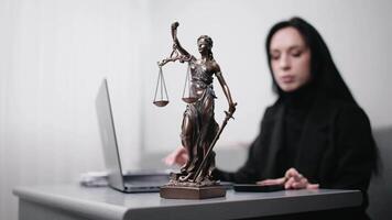 Female lawyer types on laptop makes notes in notebook, sitting at table with statue of justice in office of Themis. Business woman looks at computer screen types text, performs legal work video