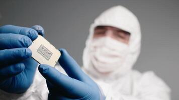 Close-up of a design engineer in a sterile jumpsuit inspecting a microchip with gloved hands in electronics factory video