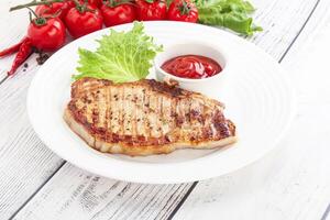 Grilled pork steak with tomato sauce and lettuce on a white plate photo