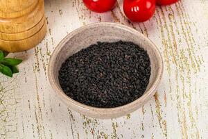 A bowl of black seeds on a table next to a bowl of tomatoes photo