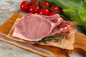 Raw pork on a cutting board with tomatoes and herbs photo