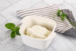 A bowl of yogurt sits on a table next to a towel photo