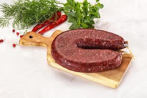A raw beef sausage on a cutting board with herbs photo