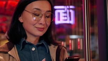 Happy smiling user positive Chinese Asian business woman girl tourist client Japanese Korean businesswoman female use mobile phone texting smartphone online app chatting message SMS outside city neon video