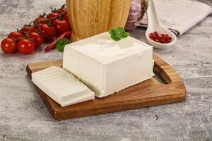 A piece of cheese on a cutting board next to tomatoes and a wooden cutting board photo