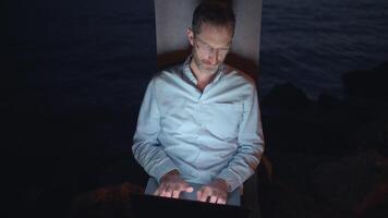 In the evening light, a dedicated man is working on his laptop at a serene waterfront video