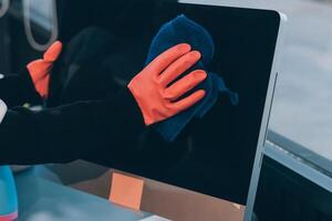 A person wearing gloves and an orange glove is cleaning a computer screen photo