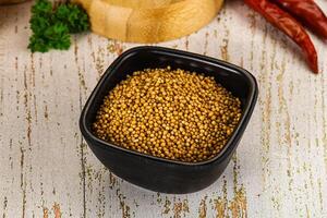 Mustard seeds in a black bowl on a wooden table photo