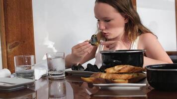 Portrait of little girl sits by table and eats tomato soup with croutons and cheese on kitchen background. Child licks fingers while eating. Kid has lunch video