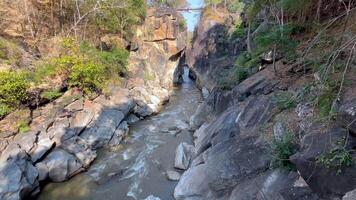 a river flowing through a narrow rocky canyon, surrounded by rugged cliffs and lush vegetation. The dynamic water movement and eroded rock formations highlight the power of nature video