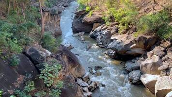 a river flowing through a narrow rocky canyon, surrounded by rugged cliffs and lush vegetation. The dynamic water movement and eroded rock formations highlight the power of nature, steep cliffs video