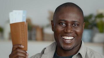 une de bonne humeur africain américain homme affiche passeport avec des billets tandis que séance dans une contemporain Accueil environnement. il apparaît détendu et confiant, mettant en valeur moderne technologie. video