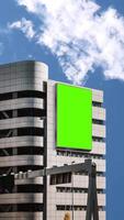 Green chroma key blank vertical billboard mock up in city center for advertising on skyscrapers with beautiful clouds portrait background video