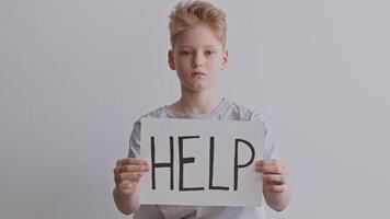 A young boy holds a sign reading help, looking serious and distressed. The setting is minimal, emphasizing his urgent plea for assistance regarding domestic violence at home. video