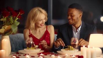 A diverse couple shares an intimate dinner at a cozy restaurant. Surrounded by candlelight and roses, they express affection and joy while enjoying their meal together. video