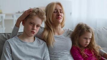 A mother sits on a couch with her two children, showing signs of distress. The family appears to be recovering from a recent episode of domestic abuse, emphasizing their emotional turmoil. video