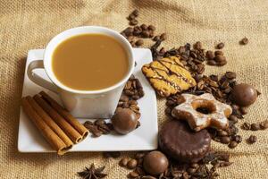 A white cup with a saucer and coffee and coffee beans on a brown cloth background. photo
