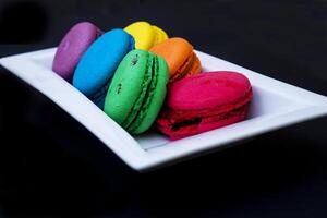 colored macaroons on a white plate on a black background photo