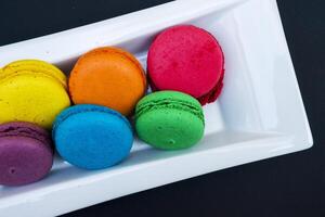 colored macaroons on a white plate on a black background photo