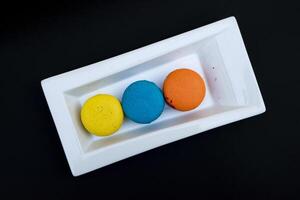 colored macaroons on a white plate on a black background photo