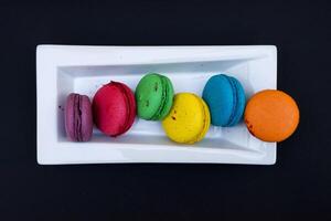 colored macaroons on a white plate on a black background photo