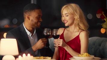 A diverse couple shares a moment of affection over dinner at a restaurant in the evening. They clink glasses while smiling, showcasing their love and connection. video