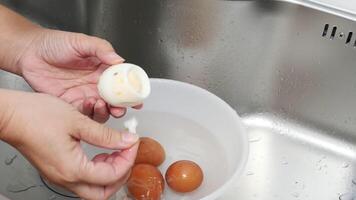 Hands Carefully Peeling Boiled Eggs Over a Bowl of Water in a Kitchen Sink, Showcasing a Simple Cooking Process with Fresh Ingredients and Clean Preparation in a Home Kitchen Setting video