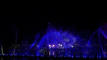 Nighttime water fountain show illuminated with vibrant blue, purple, and yellow lights, creating a stunning and colorful display with dynamic patterns against a dark backdrop video