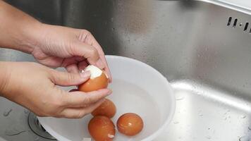 Hands Carefully Peeling Boiled Eggs Over a Bowl of Water in a Kitchen Sink, Showcasing a Simple Cooking 1Process with Fresh Ingredients and Clean Preparation in a Home Kitchen Setting video