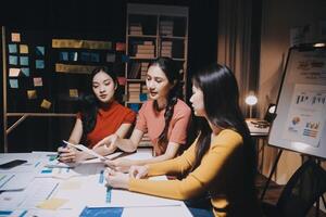 Three women sitting at a table with papers and a whiteboard photo