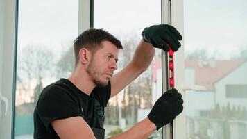 Professional builder using red spirit level for alignment of window frame during installation. Repairman adjusting white pvc windows. Concept of repair and home renovation video