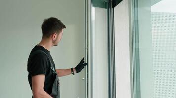 Skilled worker wearing gloves uses screwdriver to fix window frame, home renovation tasks. Professional repairman adjusting white pvc windows in modern building video