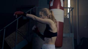 Female fighter practicing fast and strong shadow boxing hand strikes in a dark room in slow motion video