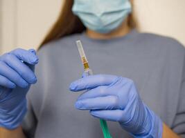 Medical professional wearing protective gear preparing vaccine injection with syringe in sterile hospital environment, focusing on precision and care while handling vaccine photo
