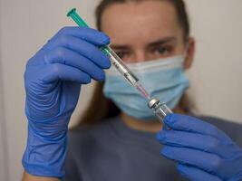 Doctor wearing blue gloves and surgical mask filling syringe with vaccine in healthcare setting, carefully preparing vaccine injection during pandemic to ensure handling of vaccine procedures. photo