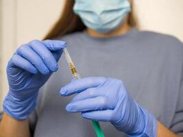 Doctor wearing blue nitrile gloves and surgical mask prepares syringe, filled with vaccine focusing on precision and safety while handling vaccine ensuring readiness for vaccine administration. photo